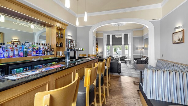 A bar area with a variety of liquor bottles, wooden chairs, and a bar counter. - Invicta Hotel (Plymouth)