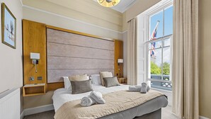 A hotel room with a large bed, a wooden headboard, a view of the city, and a window with curtains. - Invicta Hotel (Plymouth)