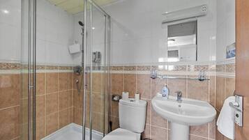 A bathroom with a glass shower enclosure, a white toilet, and a sink with a mirror above it.