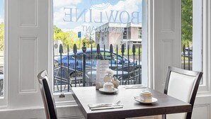 A dining table with a menu, a teapot, and a cup, set against a window with a view of a car and buildings. - Invicta Hotel (Plymouth)