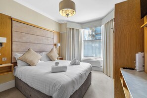 Una habitación de hotel moderna con una cama grande, cabecera de madera y vistas al exterior.