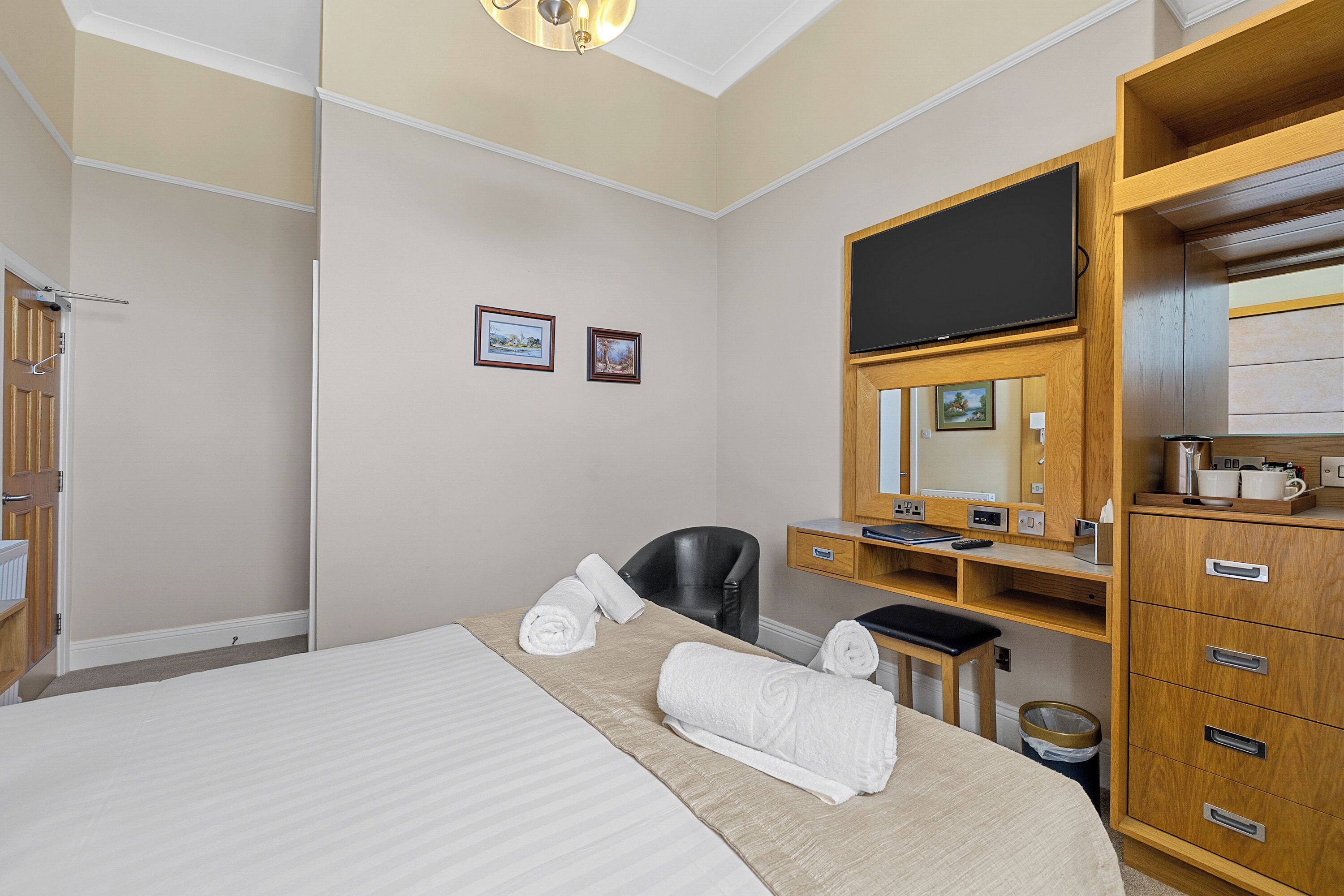 A hotel room with a bed, a desk, a chair, a television, and a wardrobe.