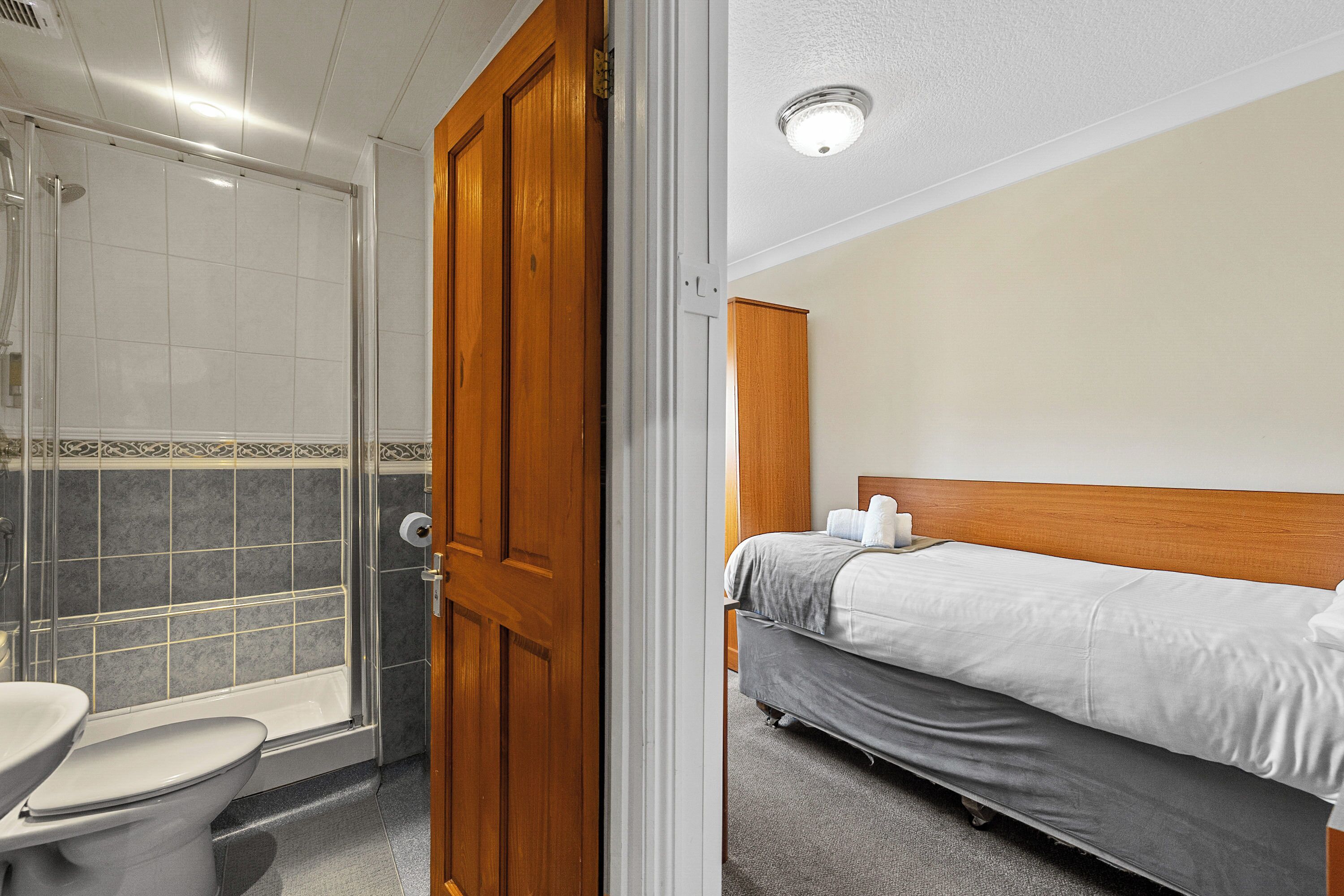 A hotel room with a shower, toilet, and a bed with a headboard.