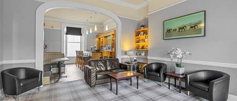 A spacious living area with a checkered carpet, leather sofas, a wooden coffee table, and a bar area in the background.