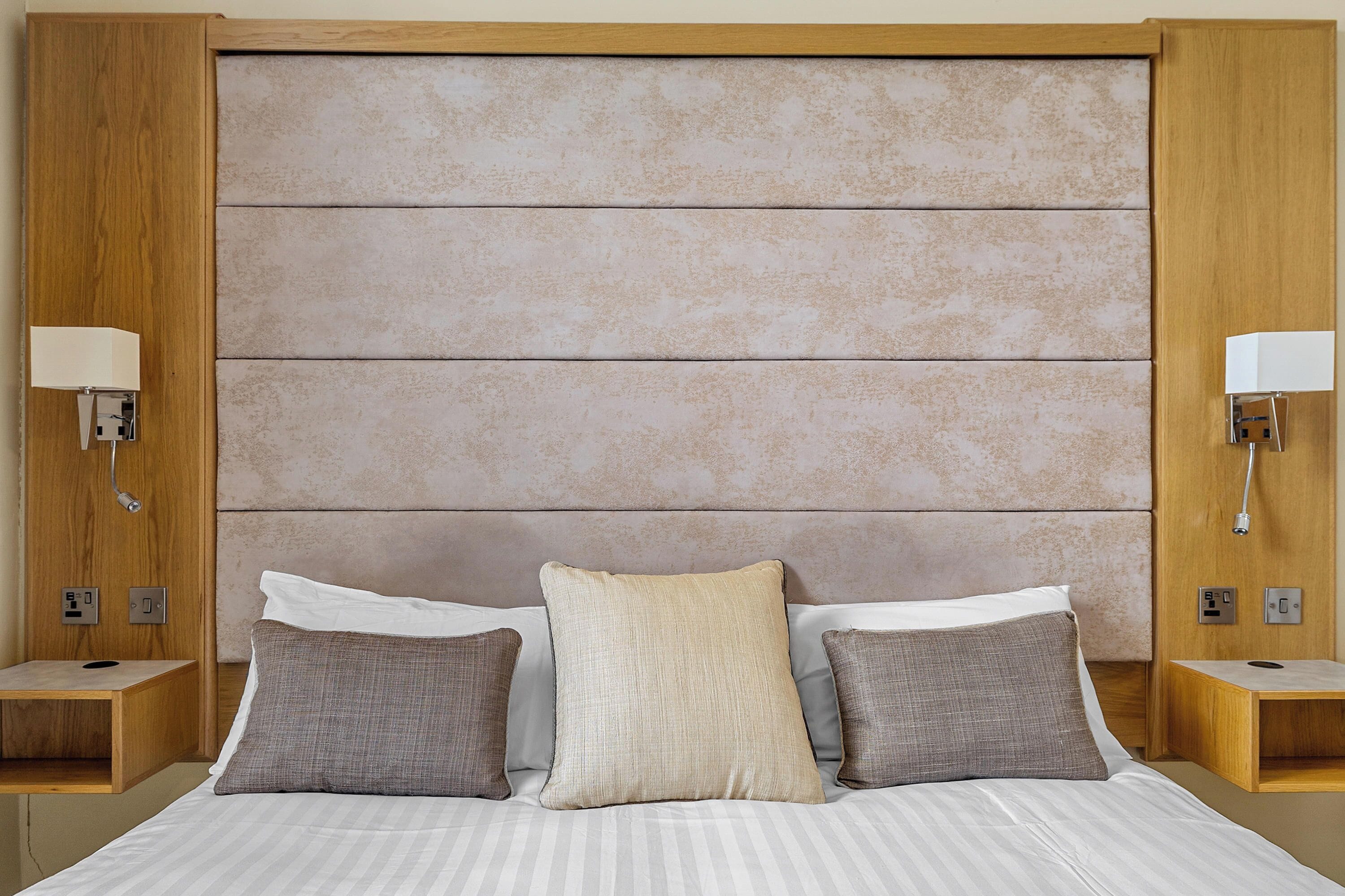 Una habitación de hotel con una cama grande, dos mesitas de noche y un cabecero con un panel texturizado.