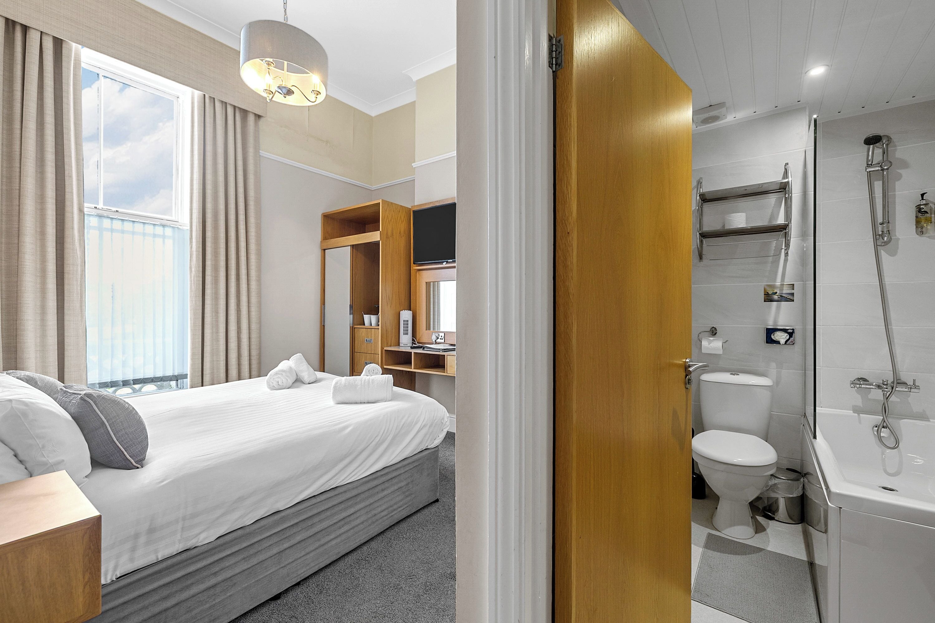 Habitación de hotel con cama, baño con ducha y vista al cielo a través de la ventana.