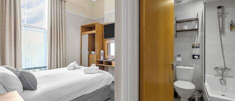 Habitación de hotel con cama, baño con ducha y vista al cielo a través de la ventana.