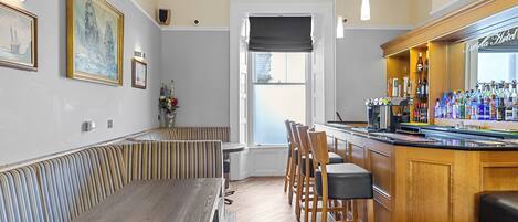 A bar area with wooden bar stools, a long counter, and a variety of bottles.