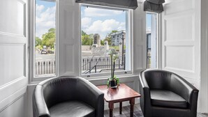 A room with two black leather chairs, a small wooden table, and a view of a street and statue through large windows. - Invicta Hotel (Plymouth)