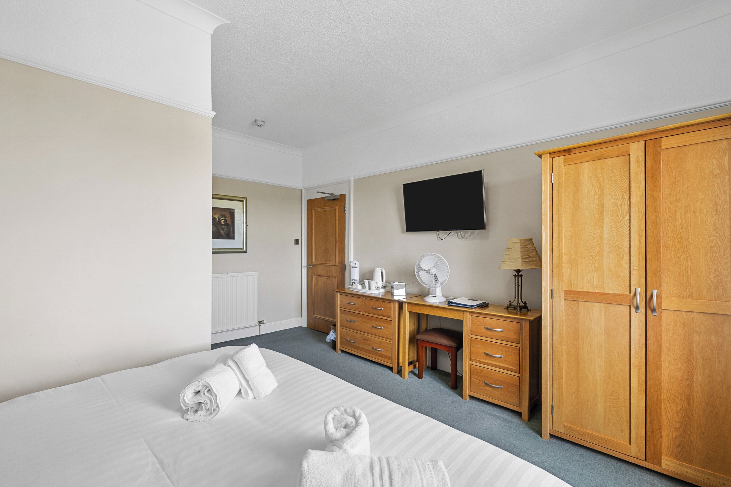 Habitación de hotel con cama, escritorio, armario, televisor y radiador.