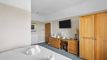 Habitación de hotel con cama, escritorio, armario, televisor y radiador.