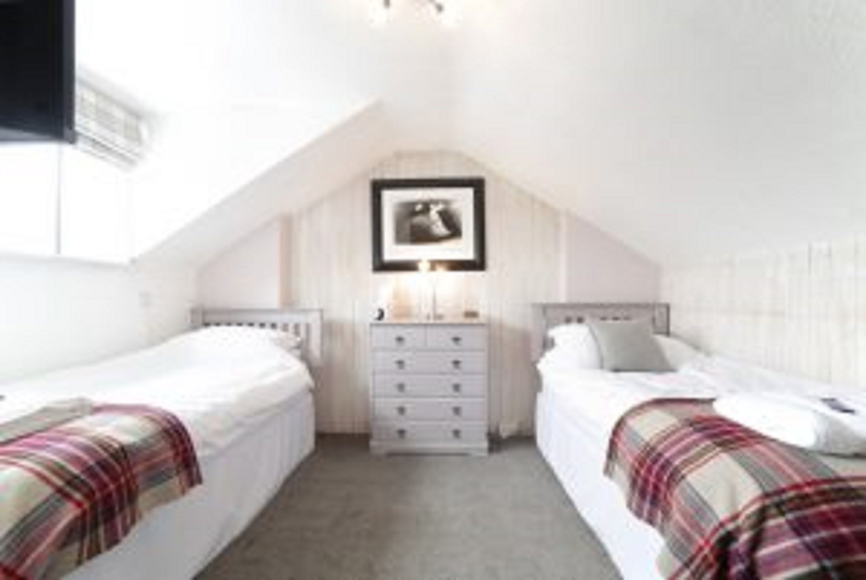 A bedroom with two beds, a dresser, and a framed picture on the wall.
