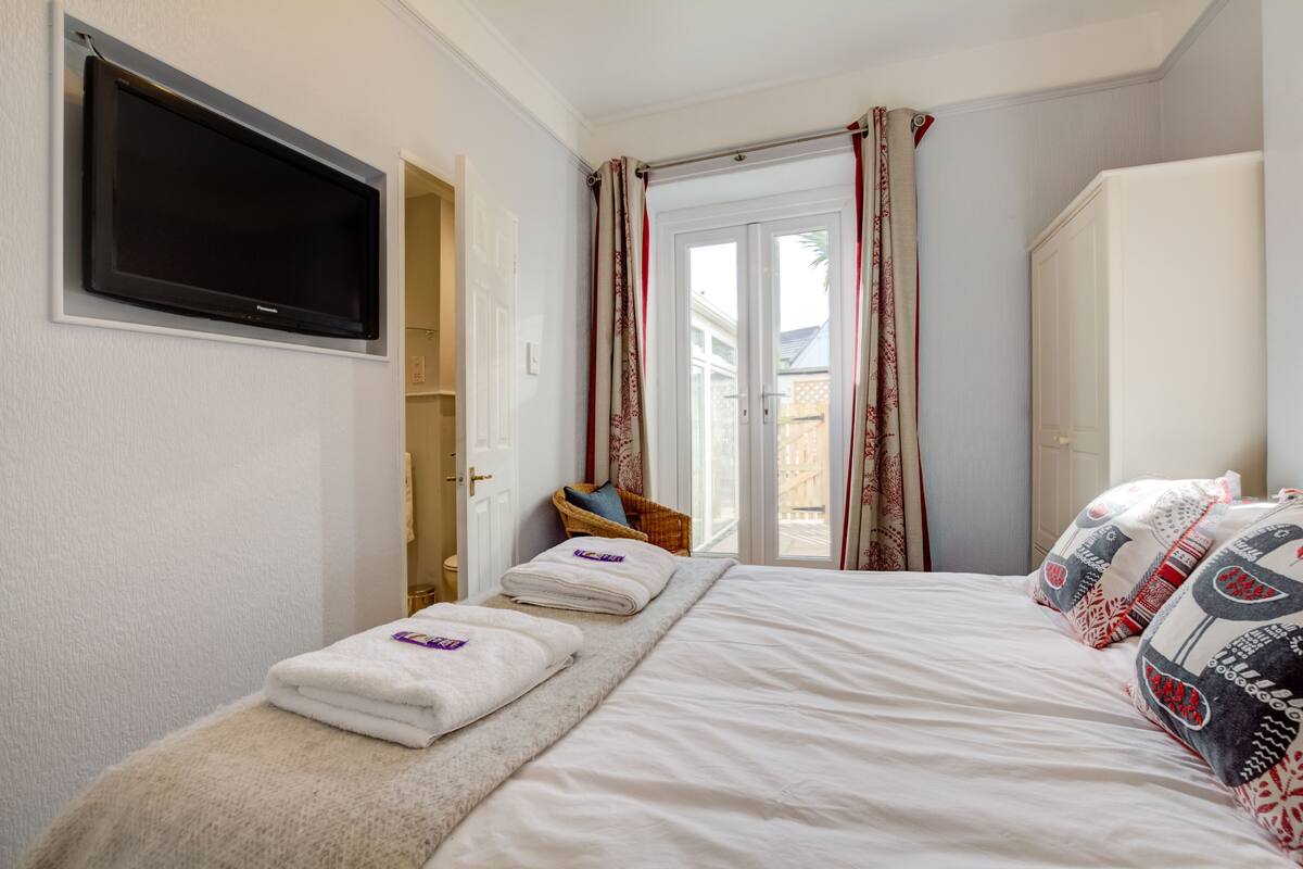 A hotel room with a bed, a TV mounted on the wall, a wardrobe, and a window with curtains.