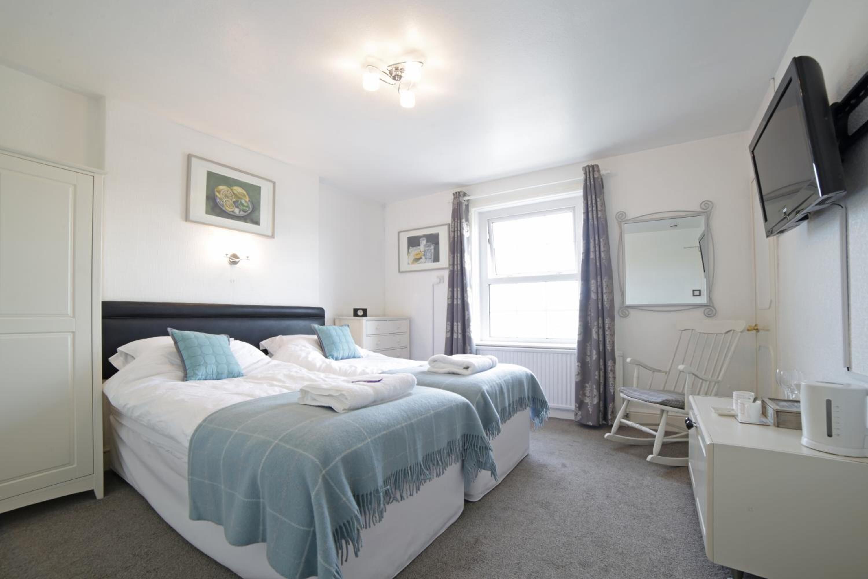 A bedroom with two beds, a TV, a desk, and a rocking chair.