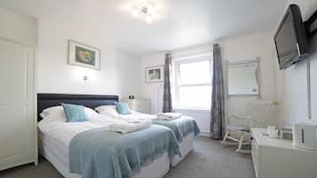 A bedroom with two beds, a TV, a desk, and a rocking chair.