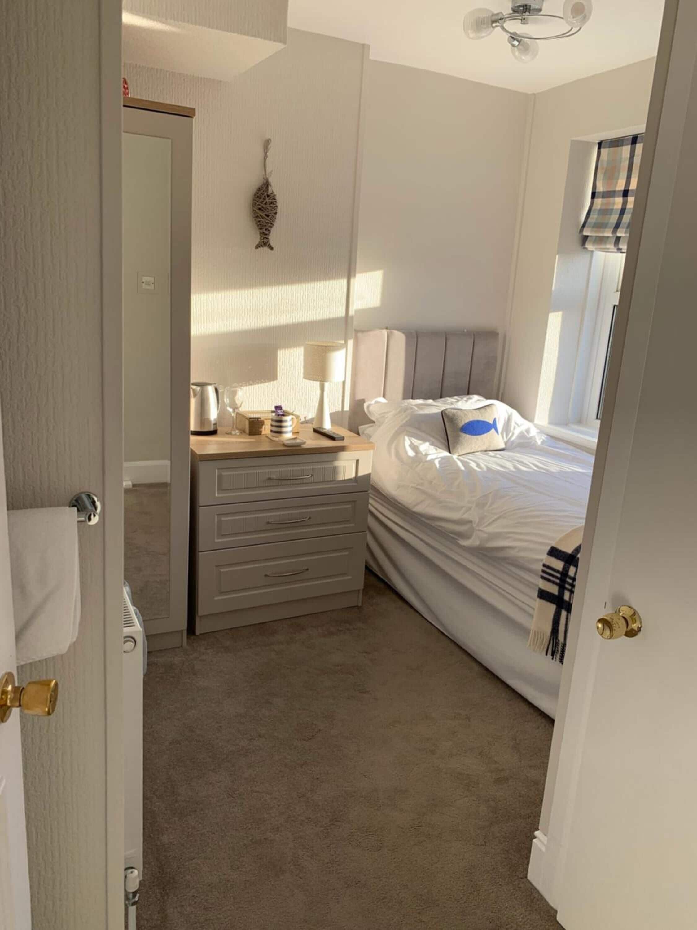 A bedroom with a bed, a dresser, a lamp, and a window.