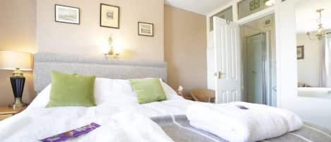 Una habitación de hotel con una cama grande, dos almohadas verdes, una manta blanca y una mesita de noche con una lámpara.