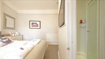 A bedroom with a bed, a bedside table, a mirror, a framed picture, and a bathroom with a glass door.