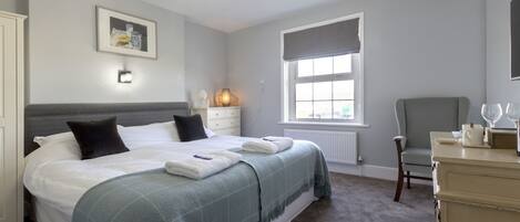 A bedroom with a bed, bedside table, lamp, chair, and window.