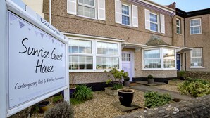 Een tweelaags huis met een bord waarop 'Sunrise Guest House' en 'Modern Bed & Breakfast Accommodatie' staat.
