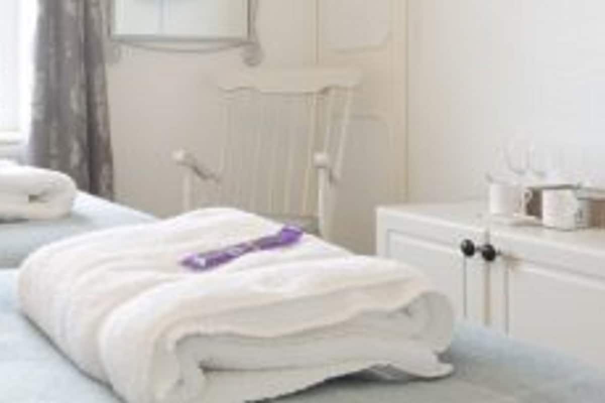 A hotel room with two beds, each with a rolled white towel and a purple item on one.