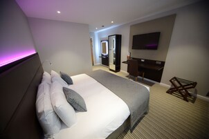 Ein Hotelzimmer mit einem großen Bett, einem Schreibtisch, einem Fernseher und einem Spiegel.