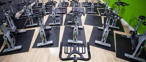 A gym with multiple stationary bikes arranged in rows on black mats, with a green wall in the background.