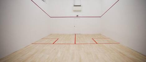 A squash court with a wooden floor and red boundary lines.