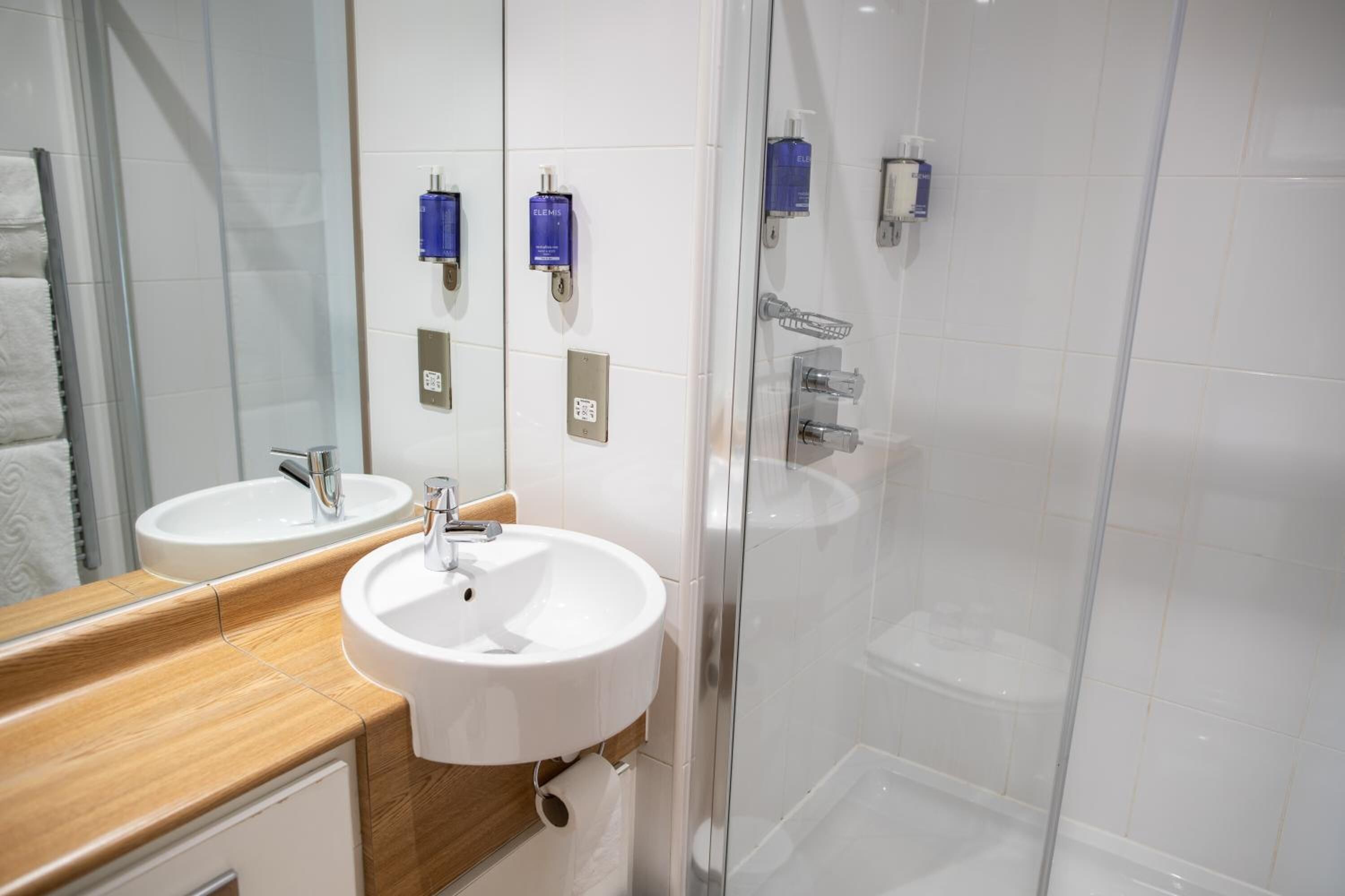 Une salle de bain moderne avec deux lavabos, un miroir et une douche à parois de verre.
