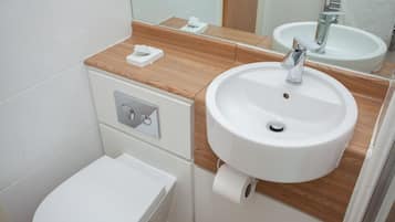 A bathroom with a white toilet, a white sink with a chrome faucet, and a wooden countertop.