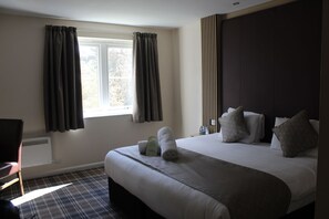 A hotel room with a large bed, a chair, a window with curtains, and a wall with vertical lines. - Hotel Bannatyne Durham (Durham)