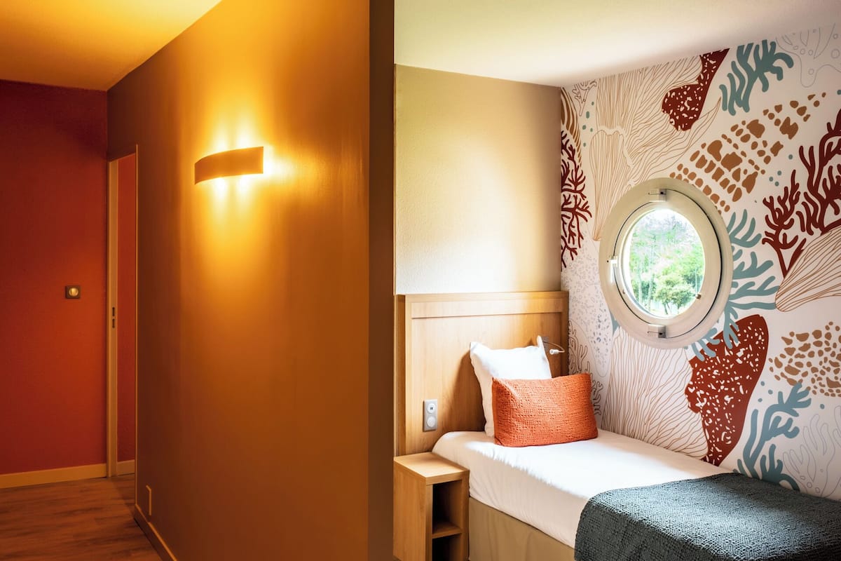 Ein Schlafzimmer mit einem hölzernen Kopfteil, einem Fenster und einer Wand mit Meeresmotiv.