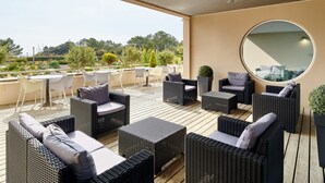 A covered outdoor seating area with wicker furniture and a round mirror on the wall. - Club Vacances Bleues Les Jardins Atlantique (Talmont-Saint-Hilaire)