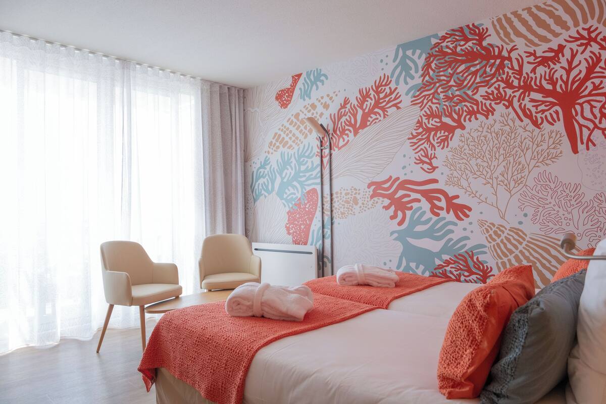 Ein Hotelzimmer mit einem Bett, zwei Stühlen, einem Nachttisch und einer Wand mit einem Korallenriff-Mural.