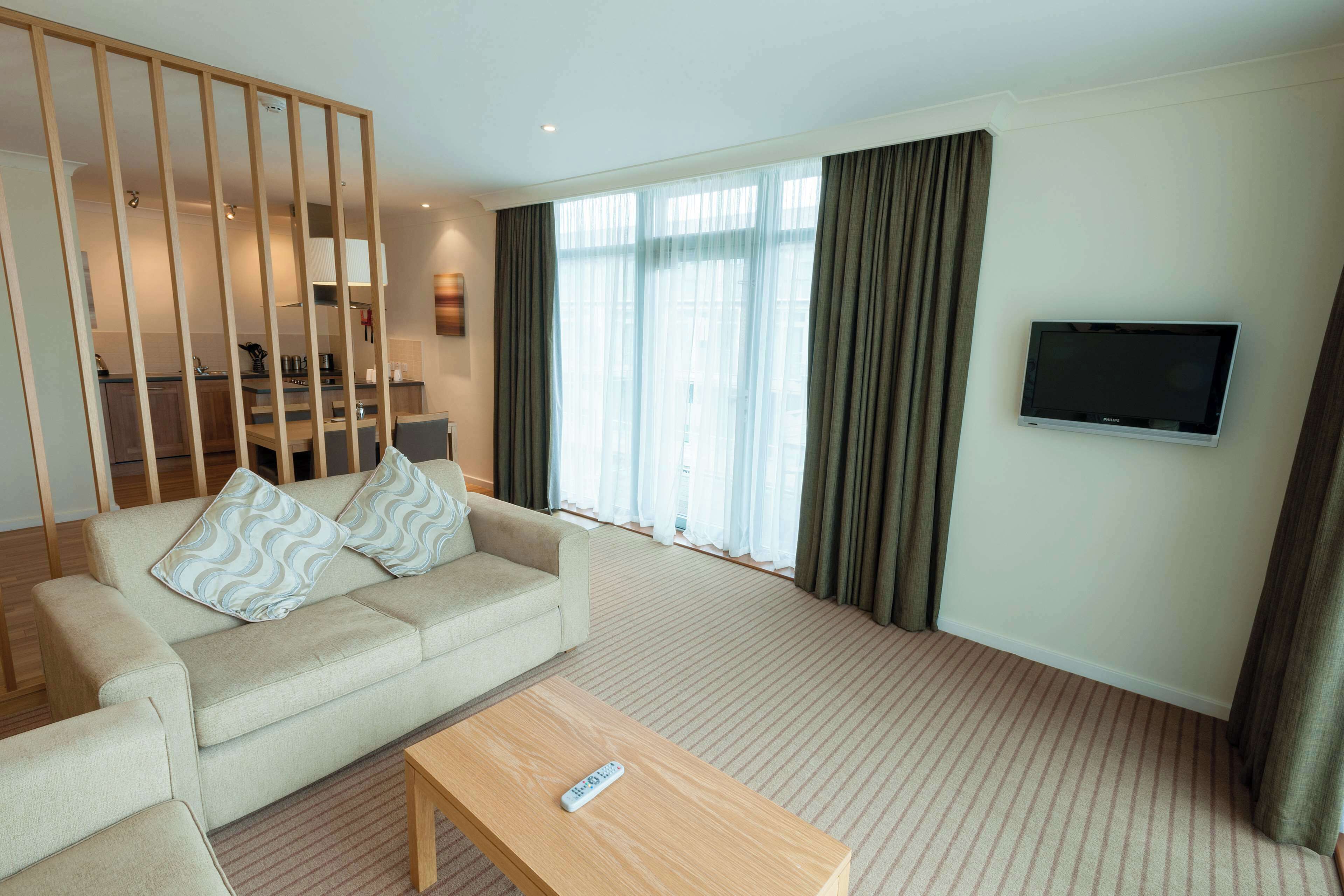 A hotel room with a sofa, a coffee table, a TV, and a large window with curtains.