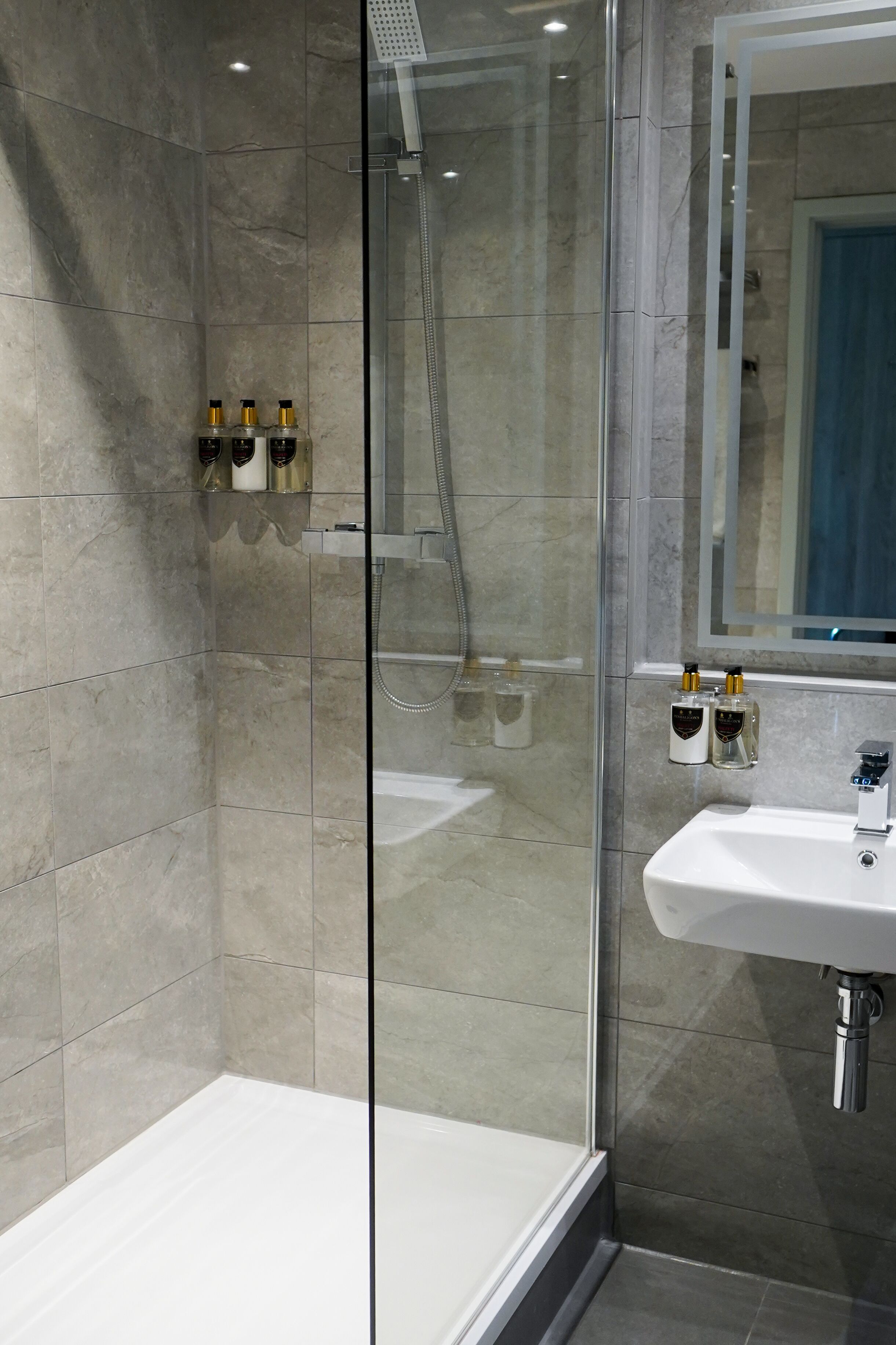 A modern bathroom with a glass-enclosed shower, a white sink, and two bottles of soap on the wall.