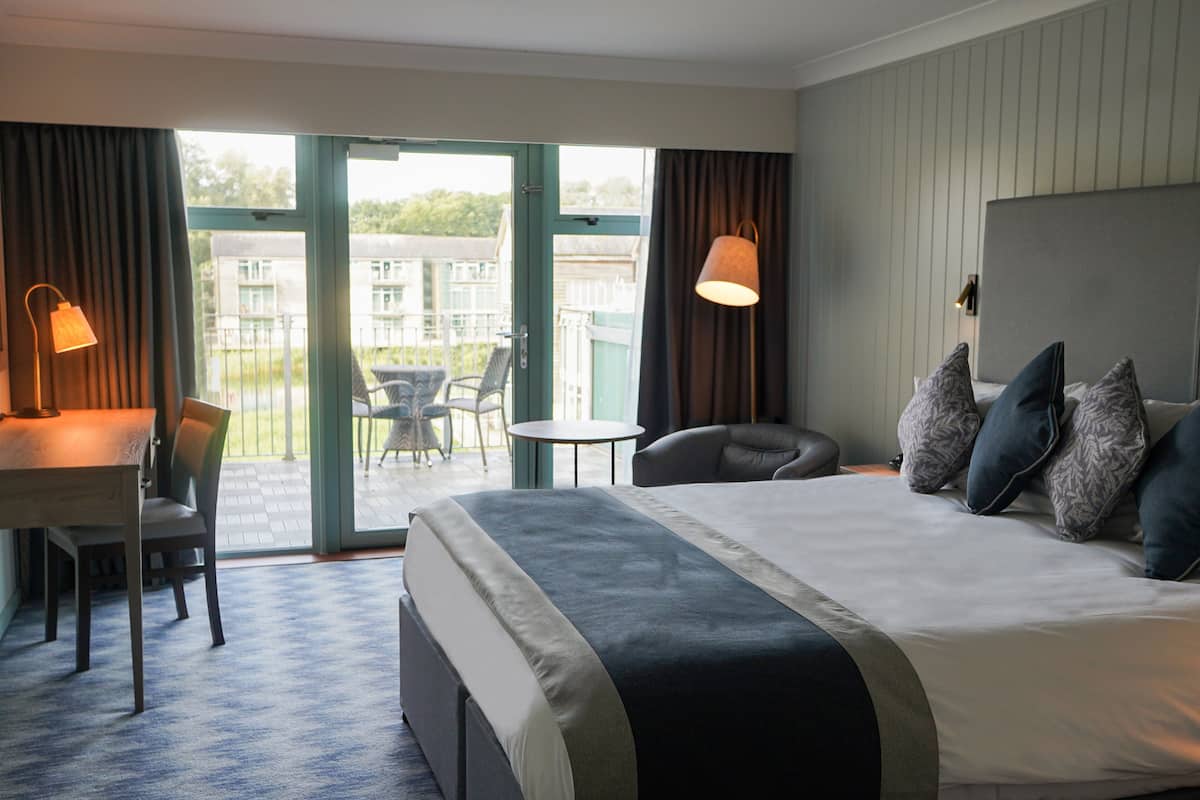 Ein Hotelzimmer mit einem großen Bett, einem Schreibtisch mit Stuhl, einem kleinen Tisch und einem Balkon mit Stuhl und Tisch.