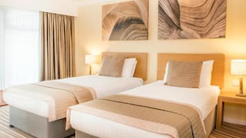Una habitación de hotel con dos camas, un ventanal con cortinas y obras de arte en las paredes.