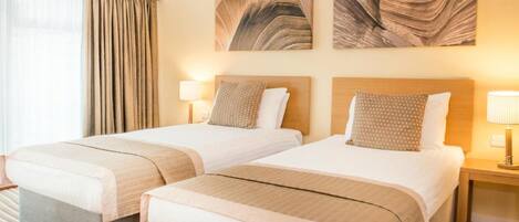 A hotel room with two beds, a large window with curtains, and artwork on the walls.