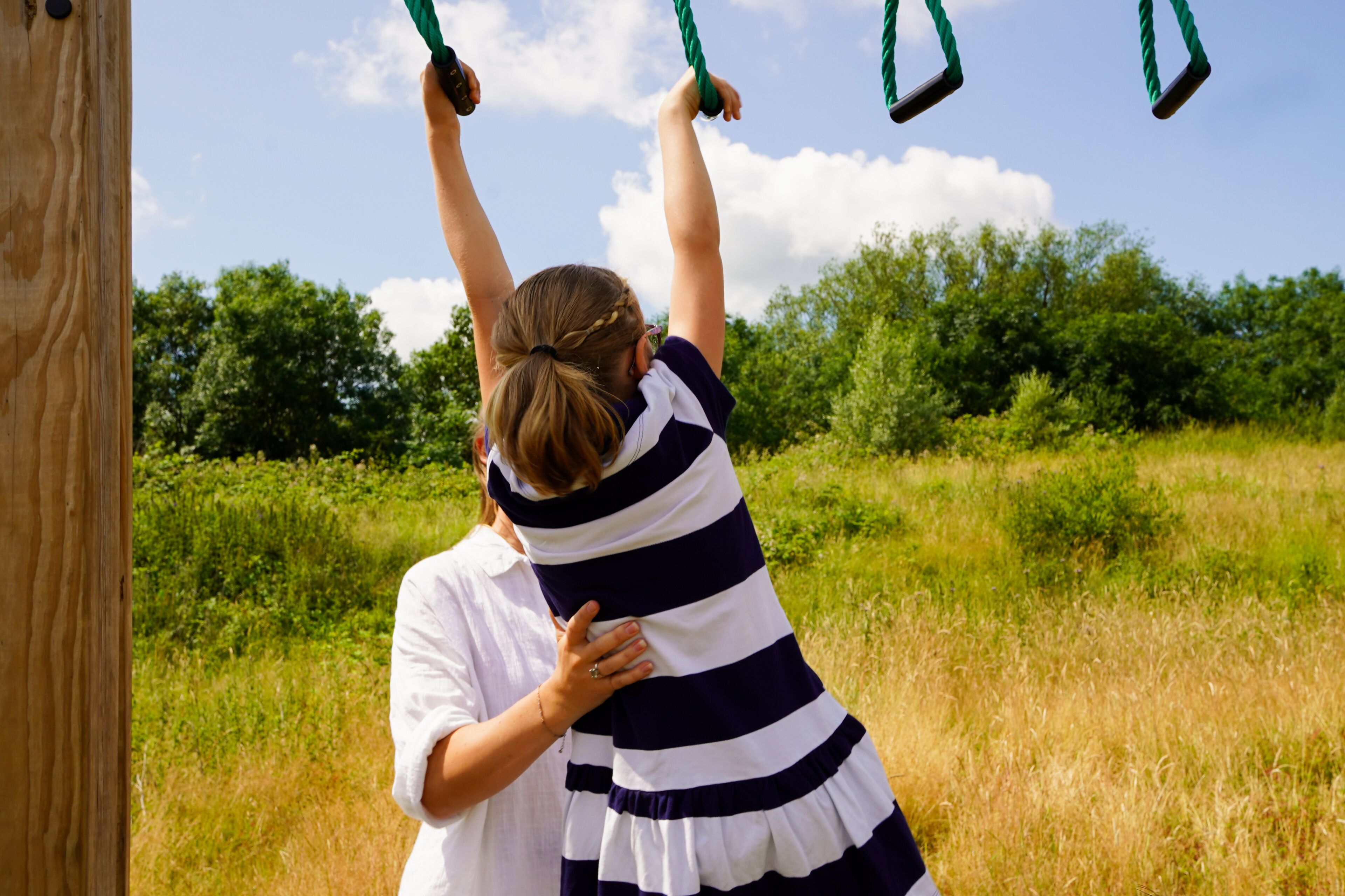 A person in a striped dress standing in a grassy field with trees in the background.