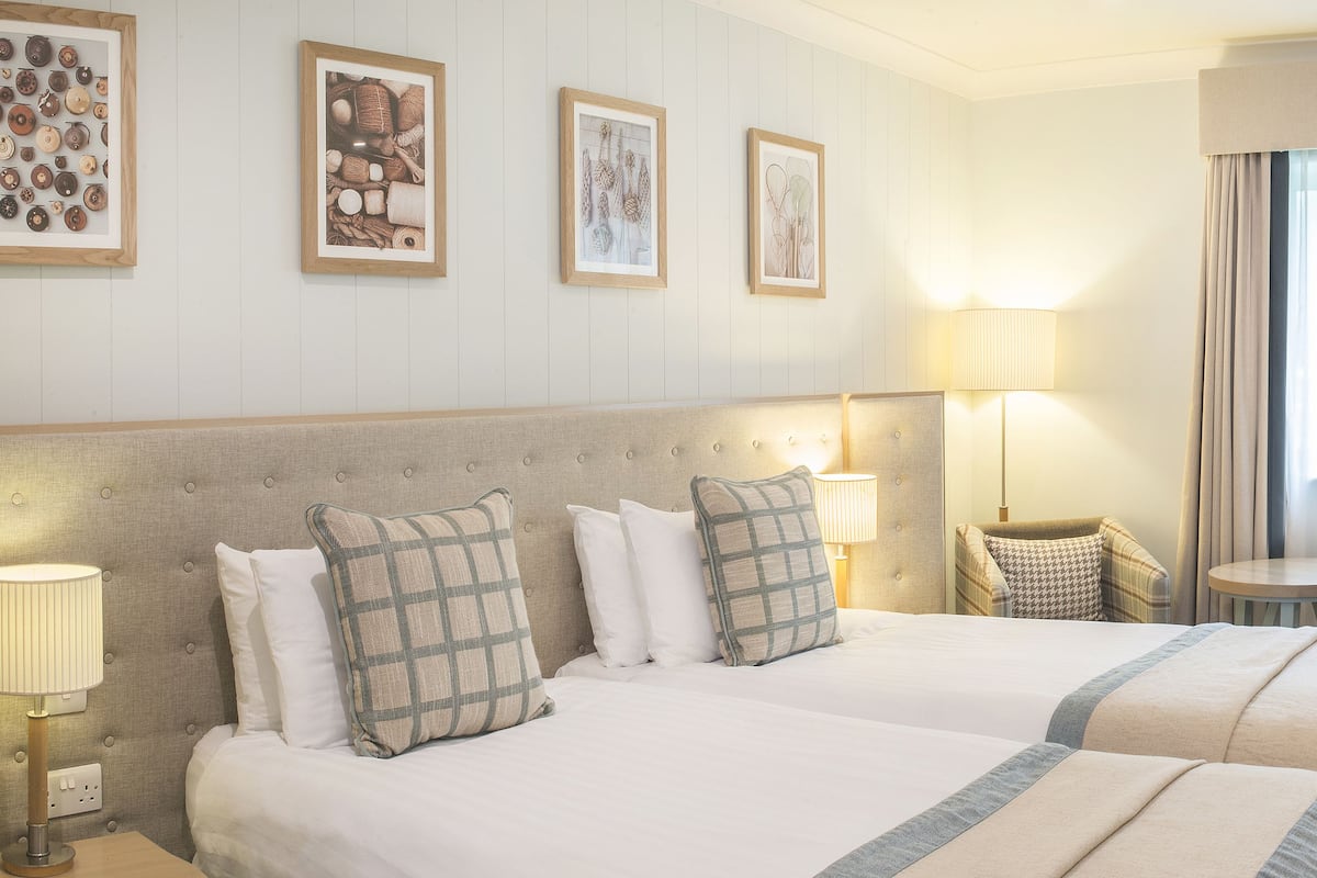 Ein Hotelzimmer mit zwei Betten, einem Schreibtisch, einem Stuhl und einer Lampe.