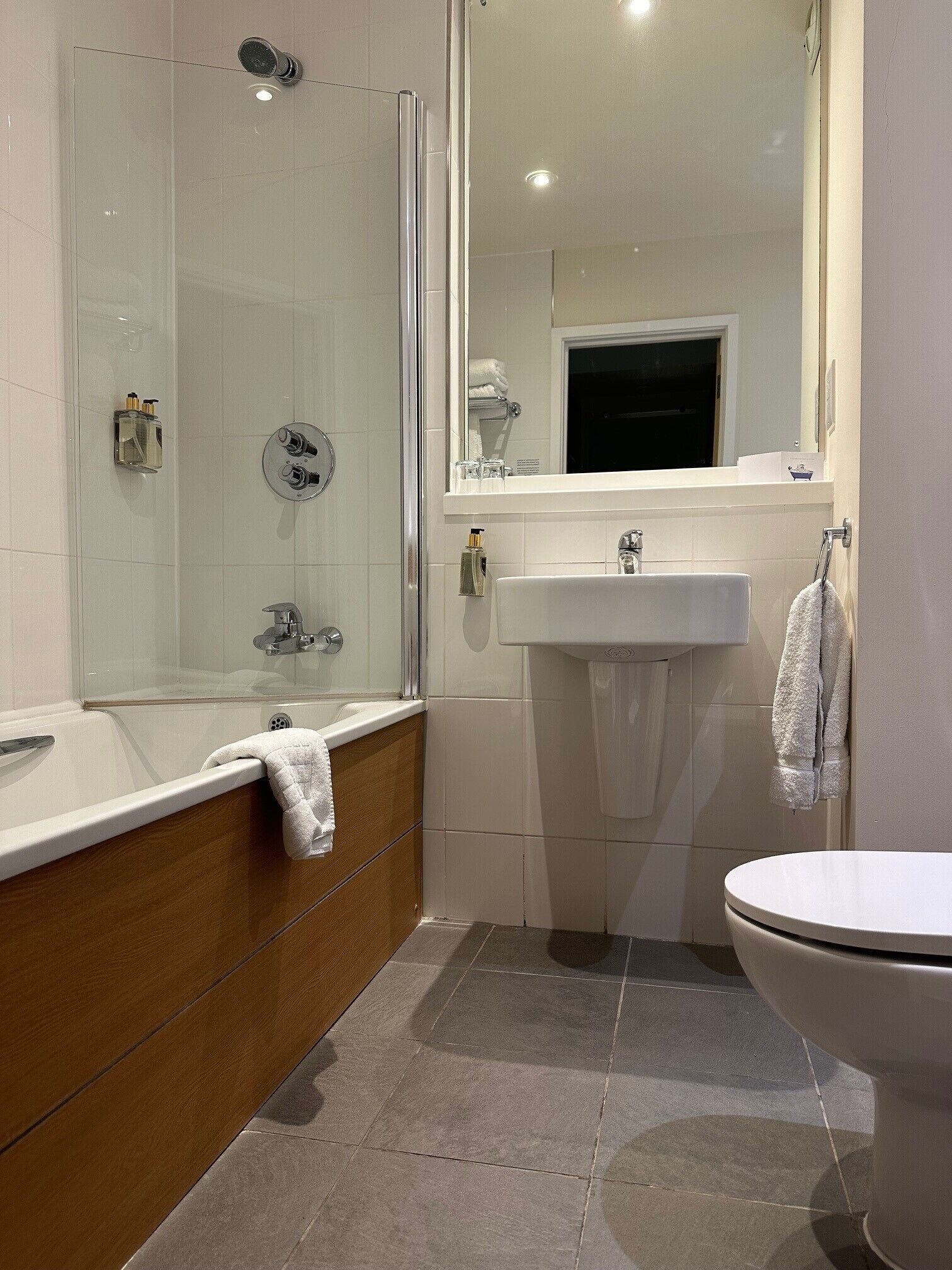 A modern bathroom with a glass-enclosed shower, a wooden vanity, a white sink, and a toilet.