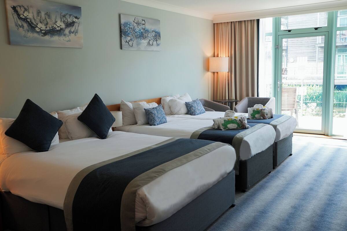 Ein Hotelzimmer mit zwei Betten, einem Schlafsofa, einer Lampe und Blick ins Freie.