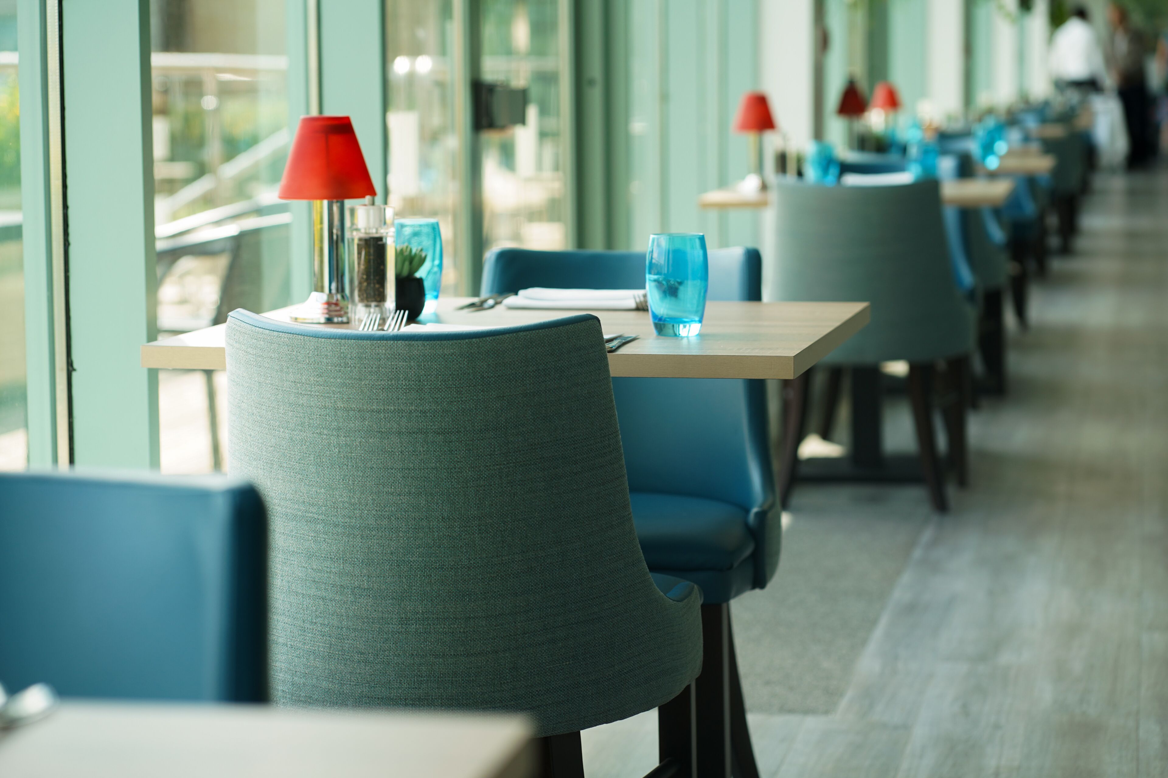 A row of tables with blue chairs and red table lamps in a restaurant setting.