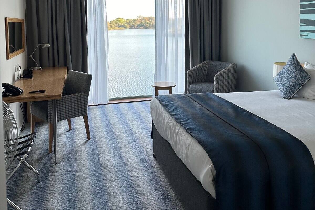 Ein Hotelzimmer mit Bett, Schreibtisch, Stuhl und Blick auf ein Gewässer.