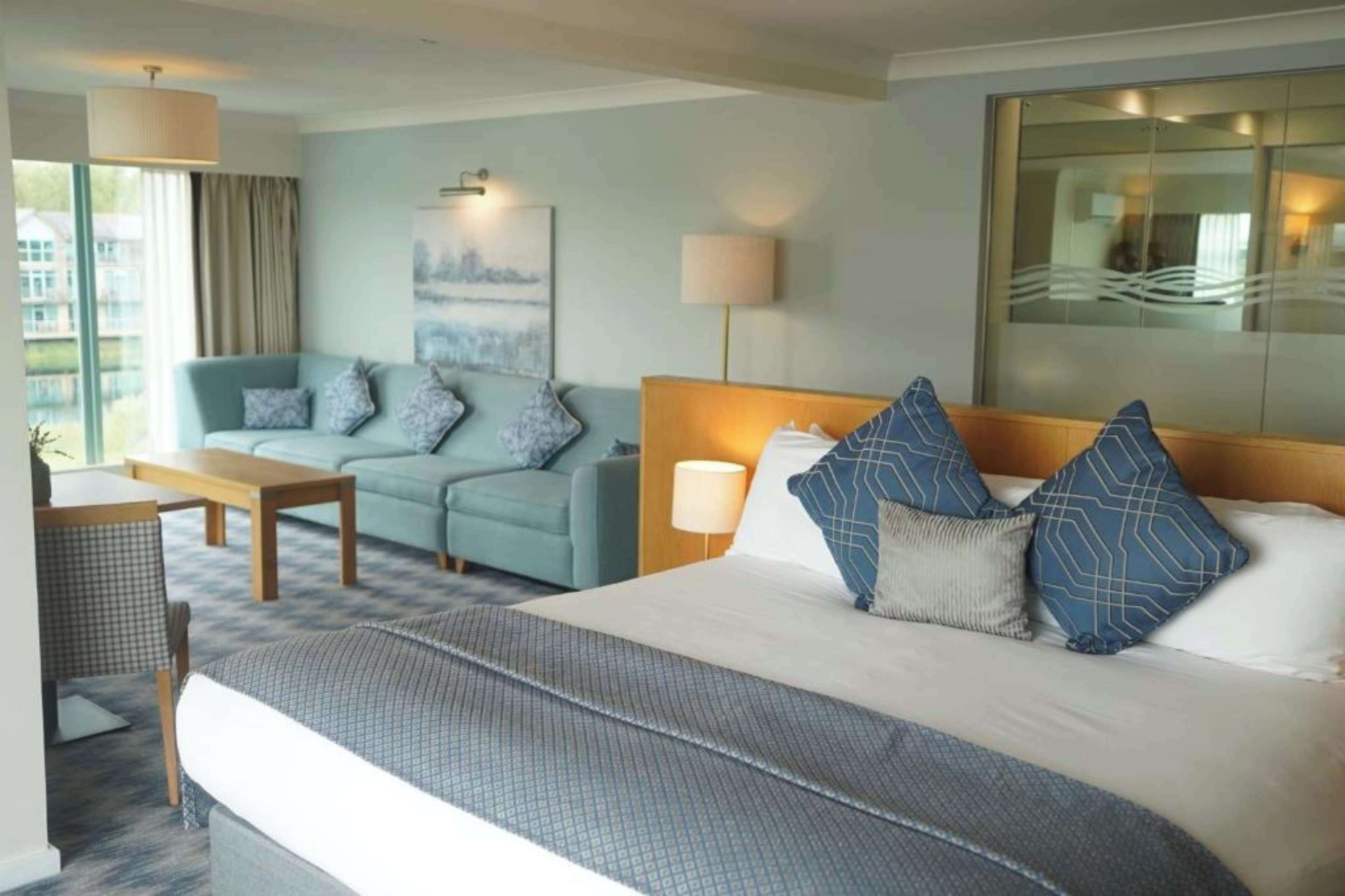A hotel room with a large bed, a sofa, a desk, and a view of the city.