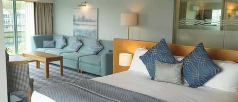 A hotel room with a large bed, a sofa, a desk, and a view of the city.