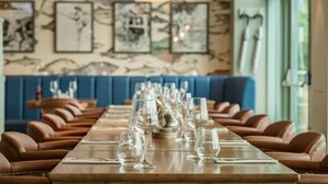 A restaurant with a long wooden table set with wine glasses and brown leather chairs. - De Vere Cotswold Water Park (Cirencester)