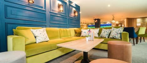 A modern lounge area with a yellow sofa, a wooden coffee table, and a bar in the background.