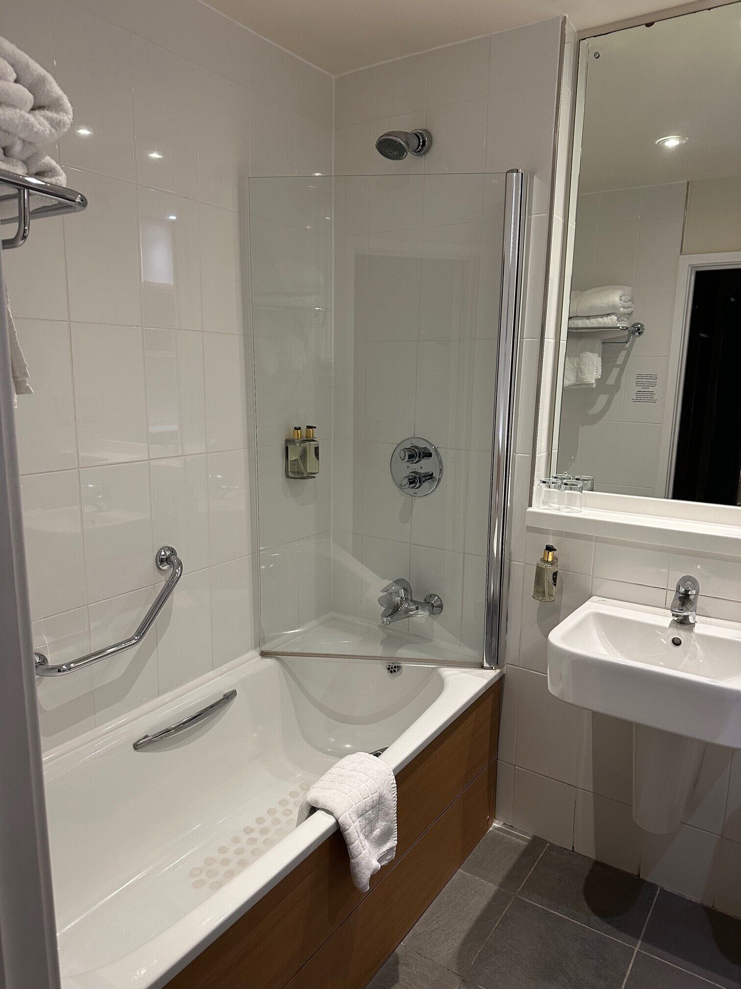 A modern bathroom with a glass-enclosed shower, a white bathtub with a towel, and a sink with a mirror.